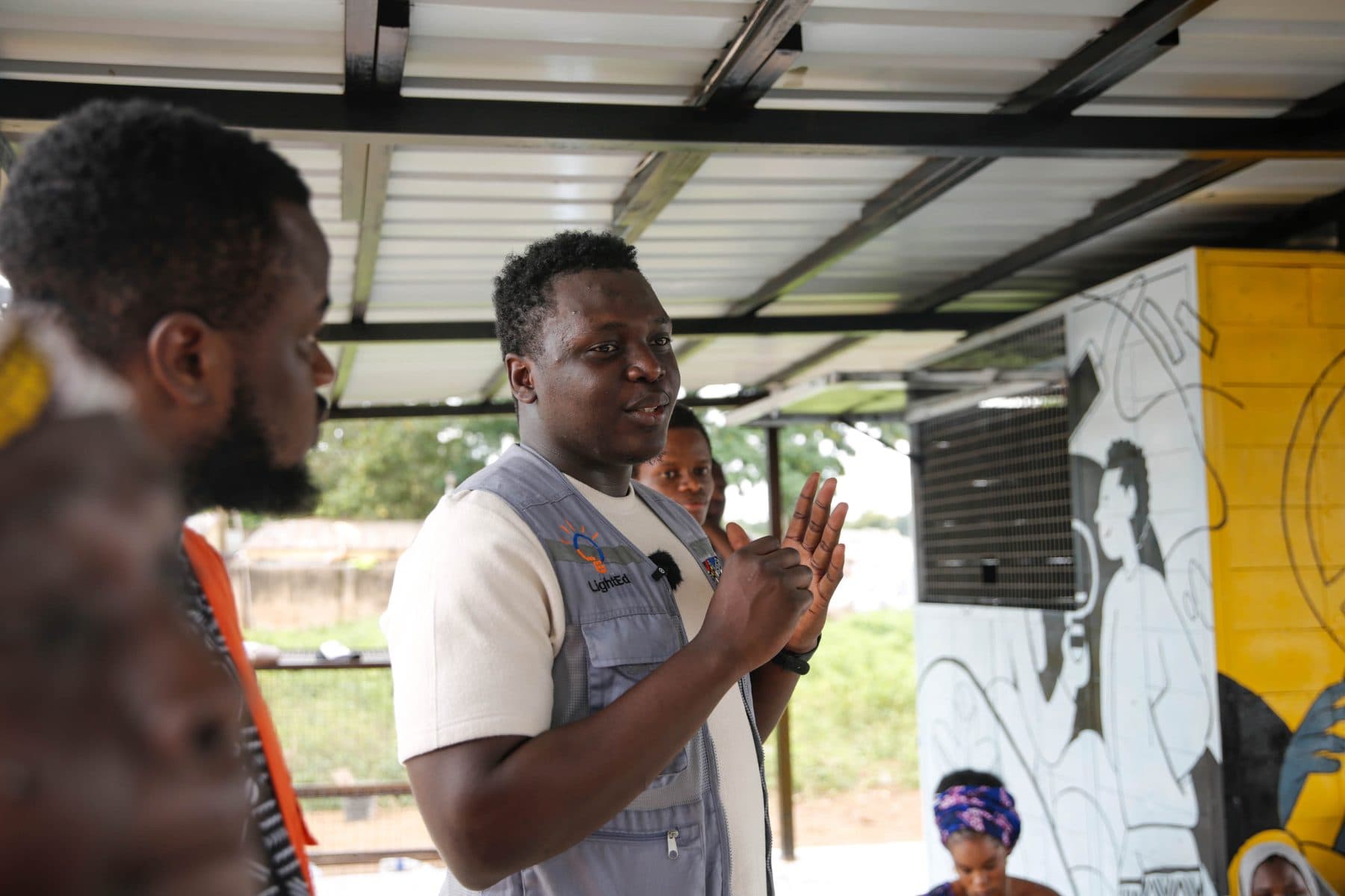 Peter speaking with a community group under a solar canopy at a LightEd site